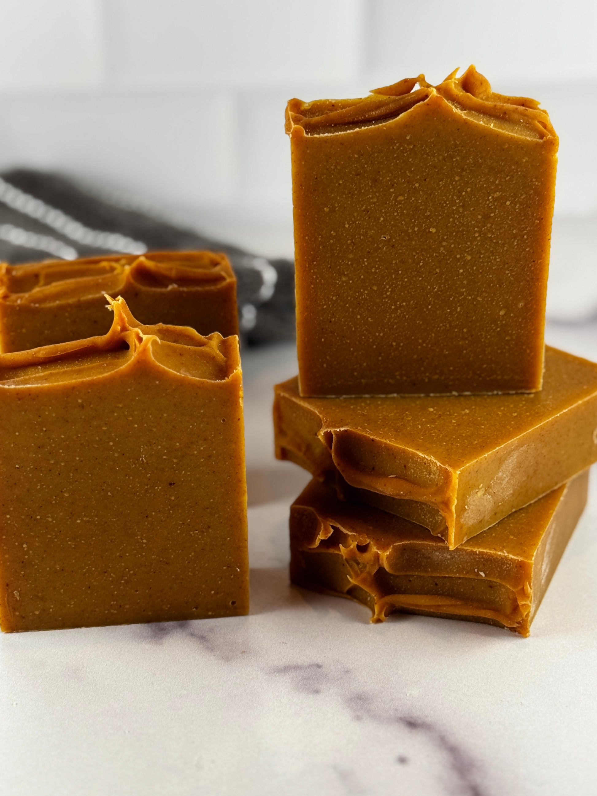 Several bars of handmade soap in a deep turmeric color, photographed on a white marble surface with a soft-focus background.