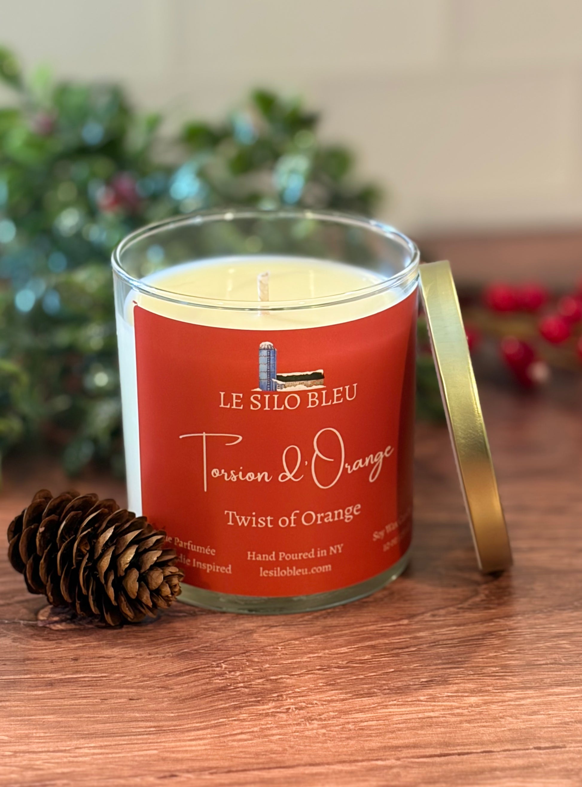 Le Silo Bleu candle Twist of Orange scent on a wooden surface with greenery and a pinecone decorative elements.