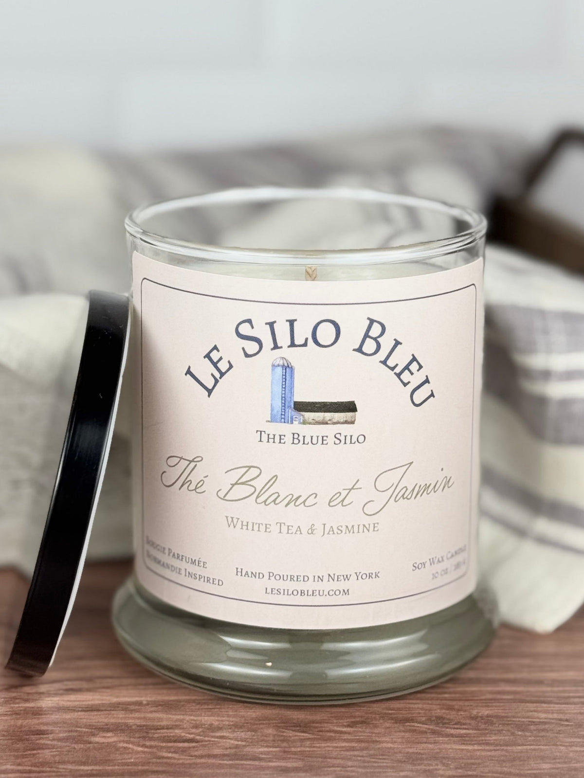 White tea and jasmine scented soy candle sitting on a wooden table with the lid next to the jar. 