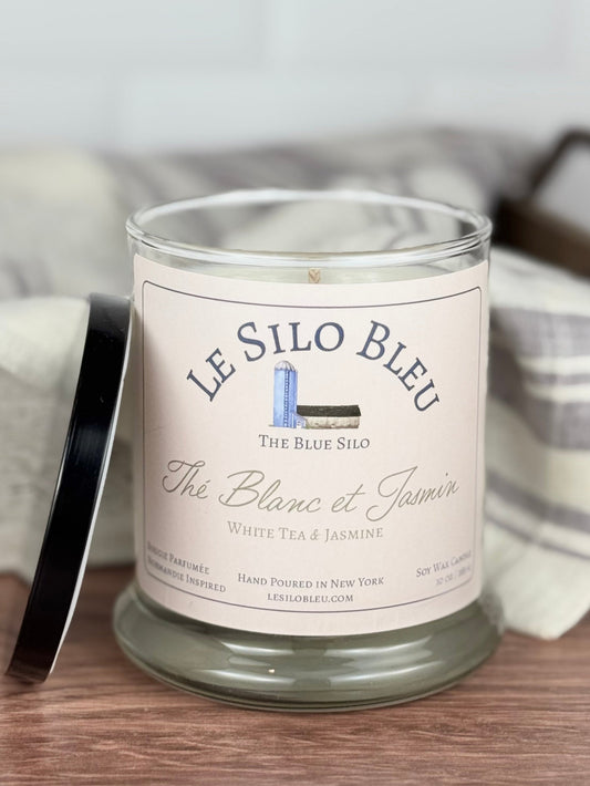 White tea and jasmine scented soy candle sitting on a wooden table with the lid next to the jar. 