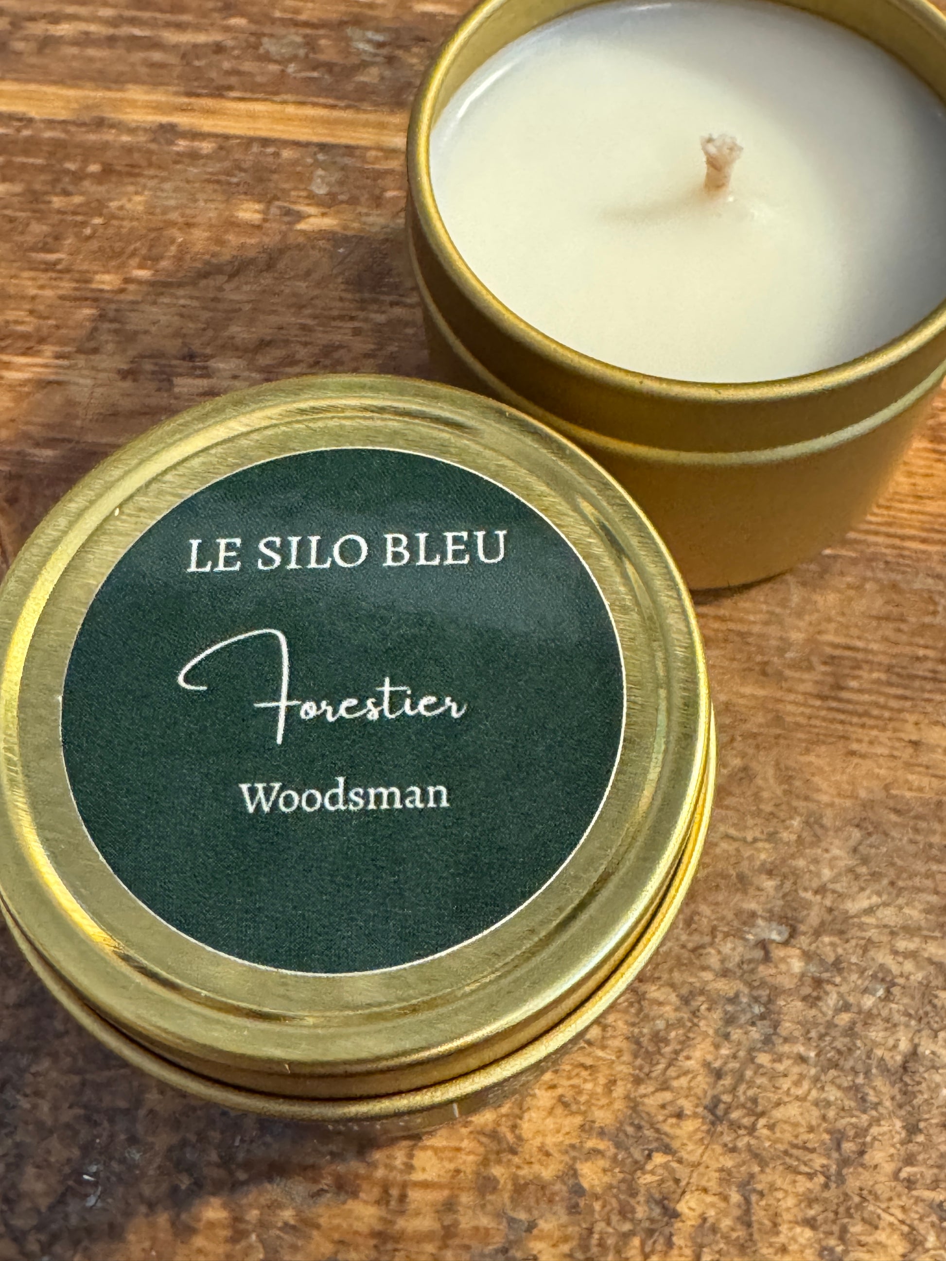 Candle in a gold tin with 'Le Silo Bleu' label on a wooden surface