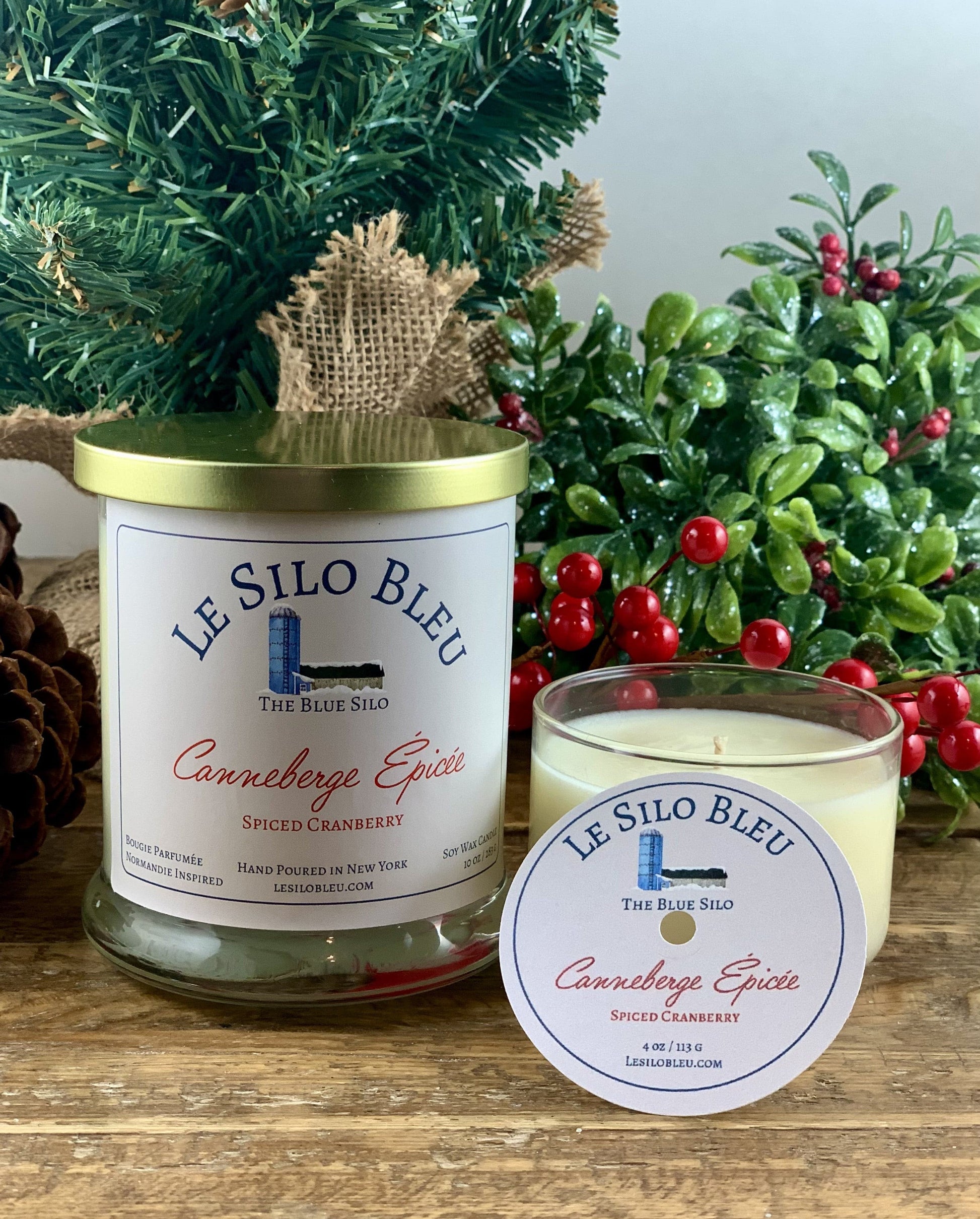 Spiced Cranberry Candles - Large and Small sizes sitting on a wooden table with christmas decorations of pinecones, fir branches and holly berries in the background.