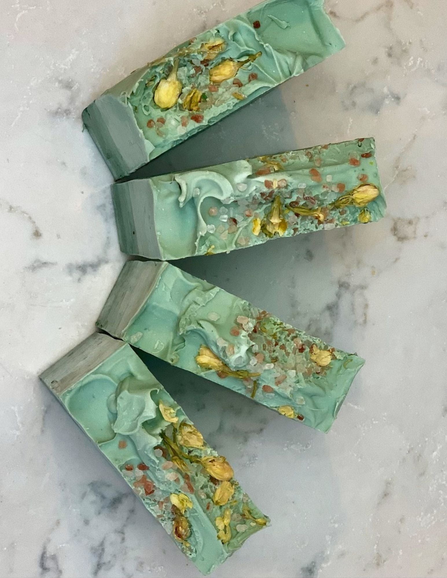 Soft Eucalyptus Soap on a white marble countertop with Jasmine Flowers and Pink Sea Salt. This is an ombre soap from dark green on the bottom to light green.